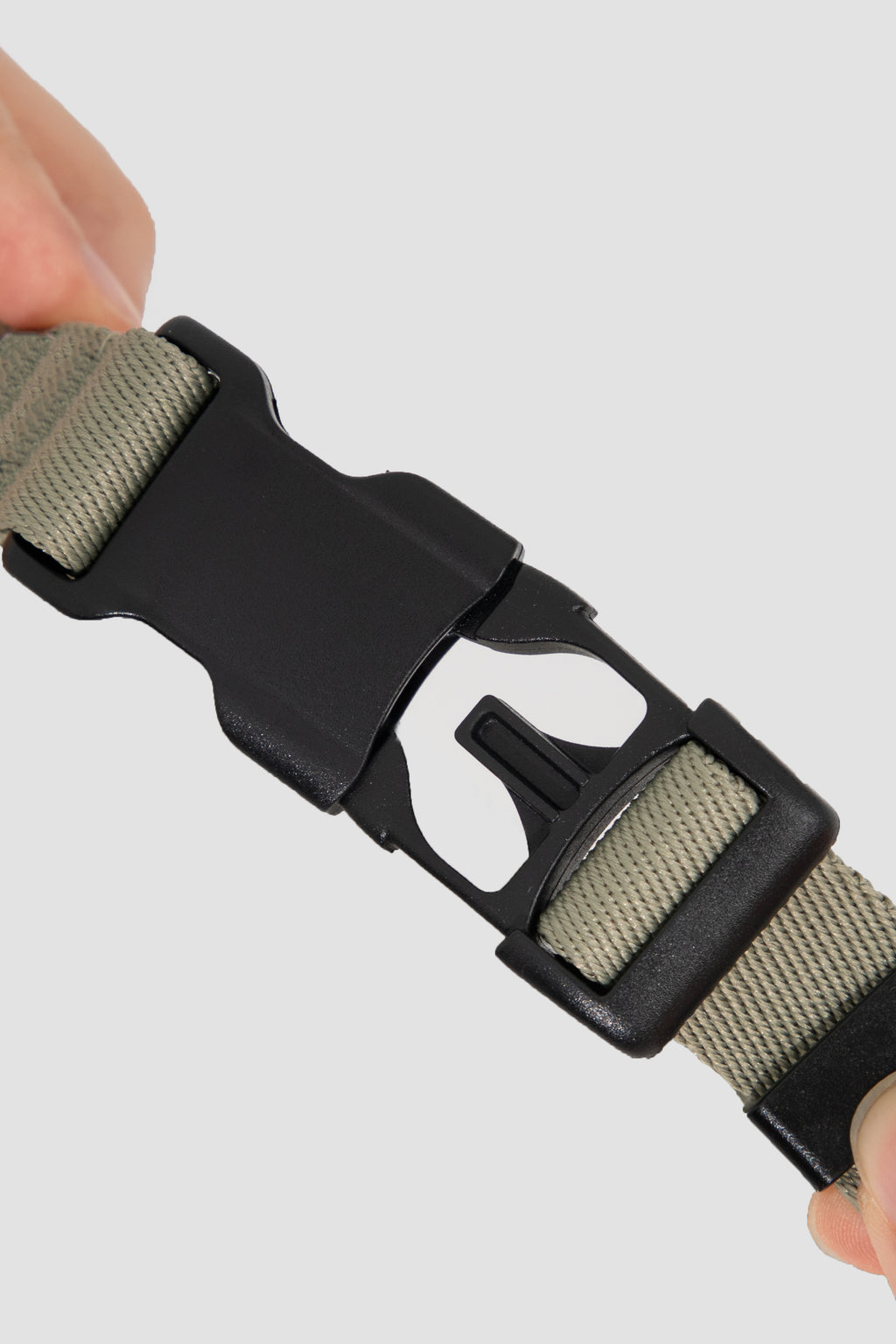 Close-up of a olive green belt with a black buckle held by a hand on a light gray background