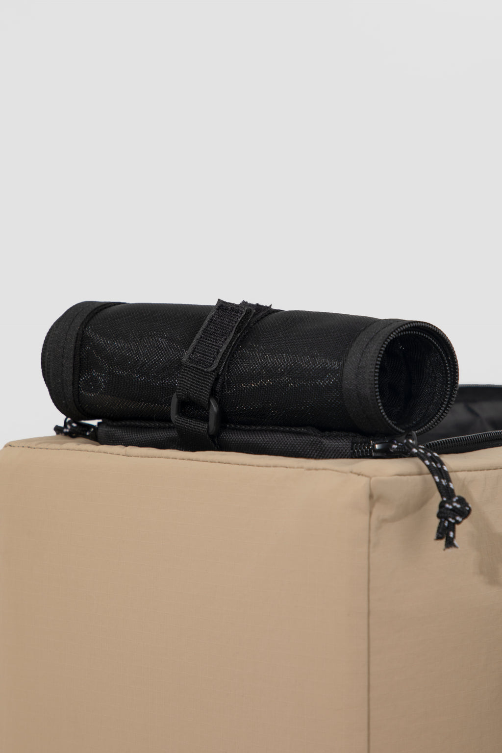 A black rolled-up fabric mat or yoga mat secured with a black strap, resting on top of a beige box against a light gray background.