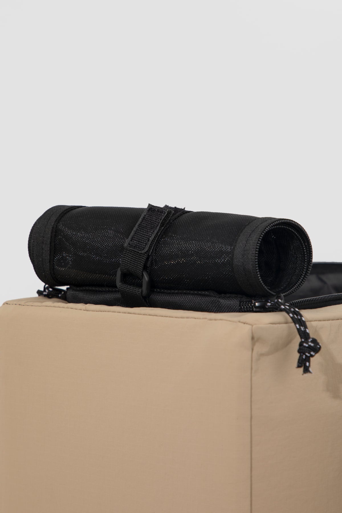 A black rolled-up fabric mat or yoga mat secured with a black strap, resting on top of a beige box against a light gray background.