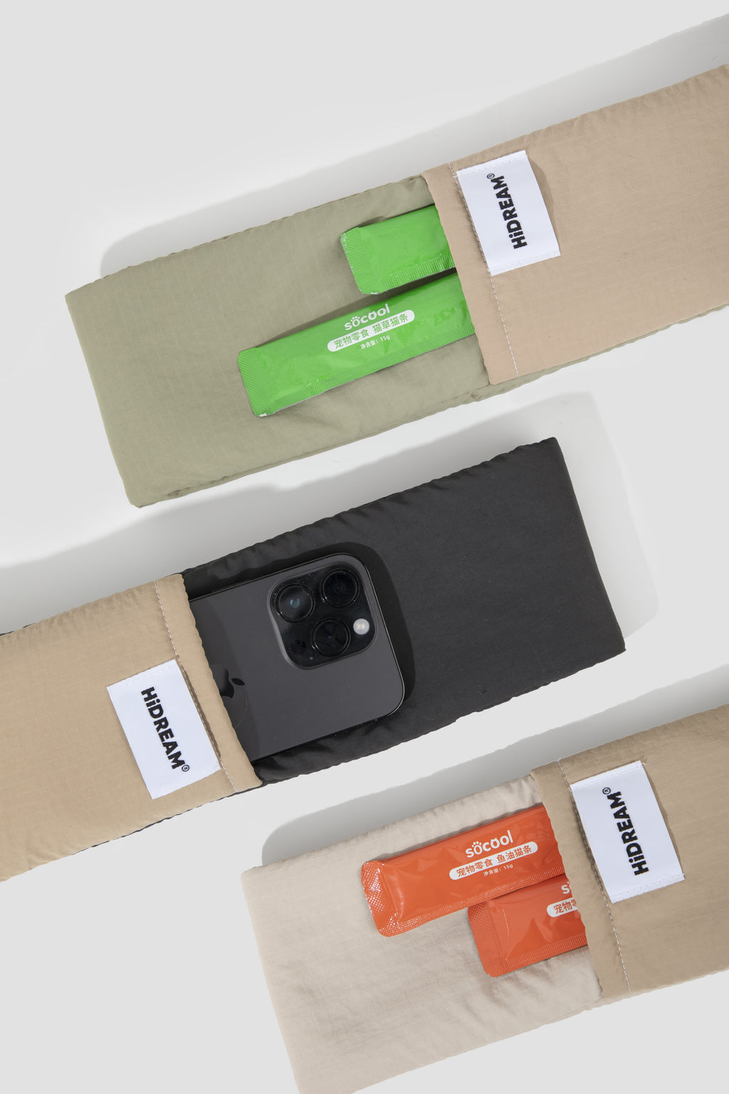 Three beige fabric pouches with white 'HiDREAM' labels are arranged diagonally on a white background. The top pouch contains green packets, the middle pouch holds a black smartphone, and the bottom pouch contains orange packets.