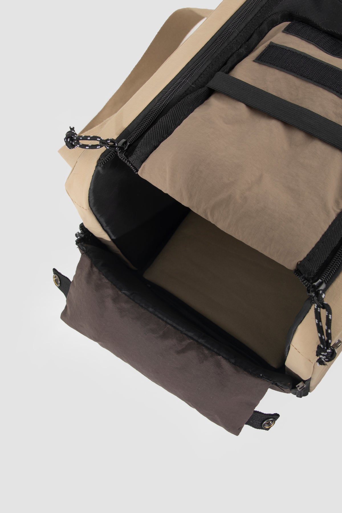 Close-up of a beige and black backpack showing the interior compartments, zipper details, and webbing straps against a light gray background.