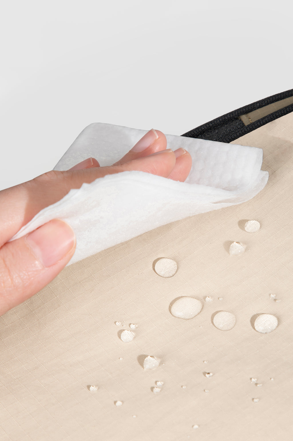 Hand using a white cloth to clean a beige surface with water droplets.