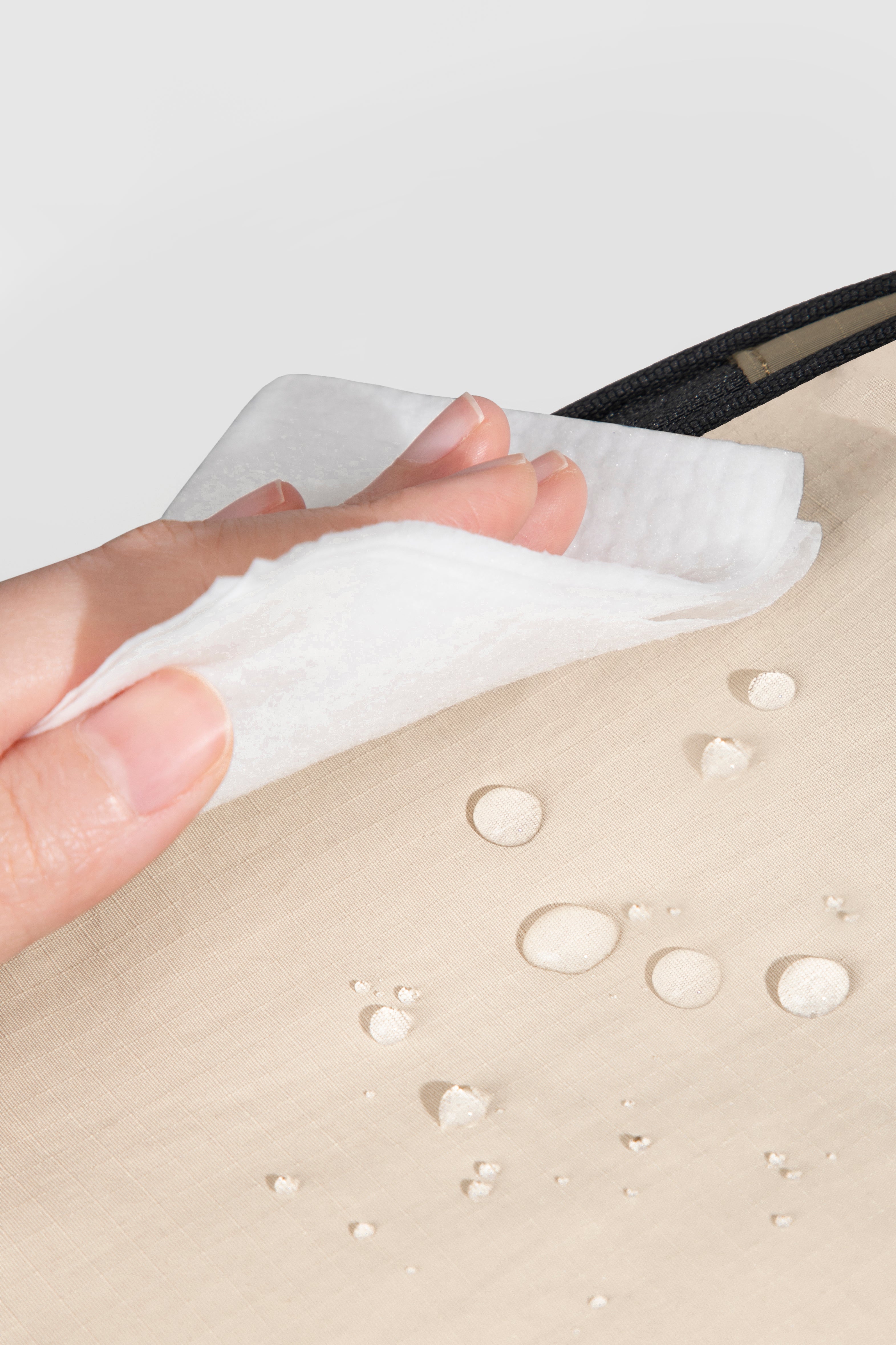 Hand using a white cloth to clean a beige surface with water droplets.