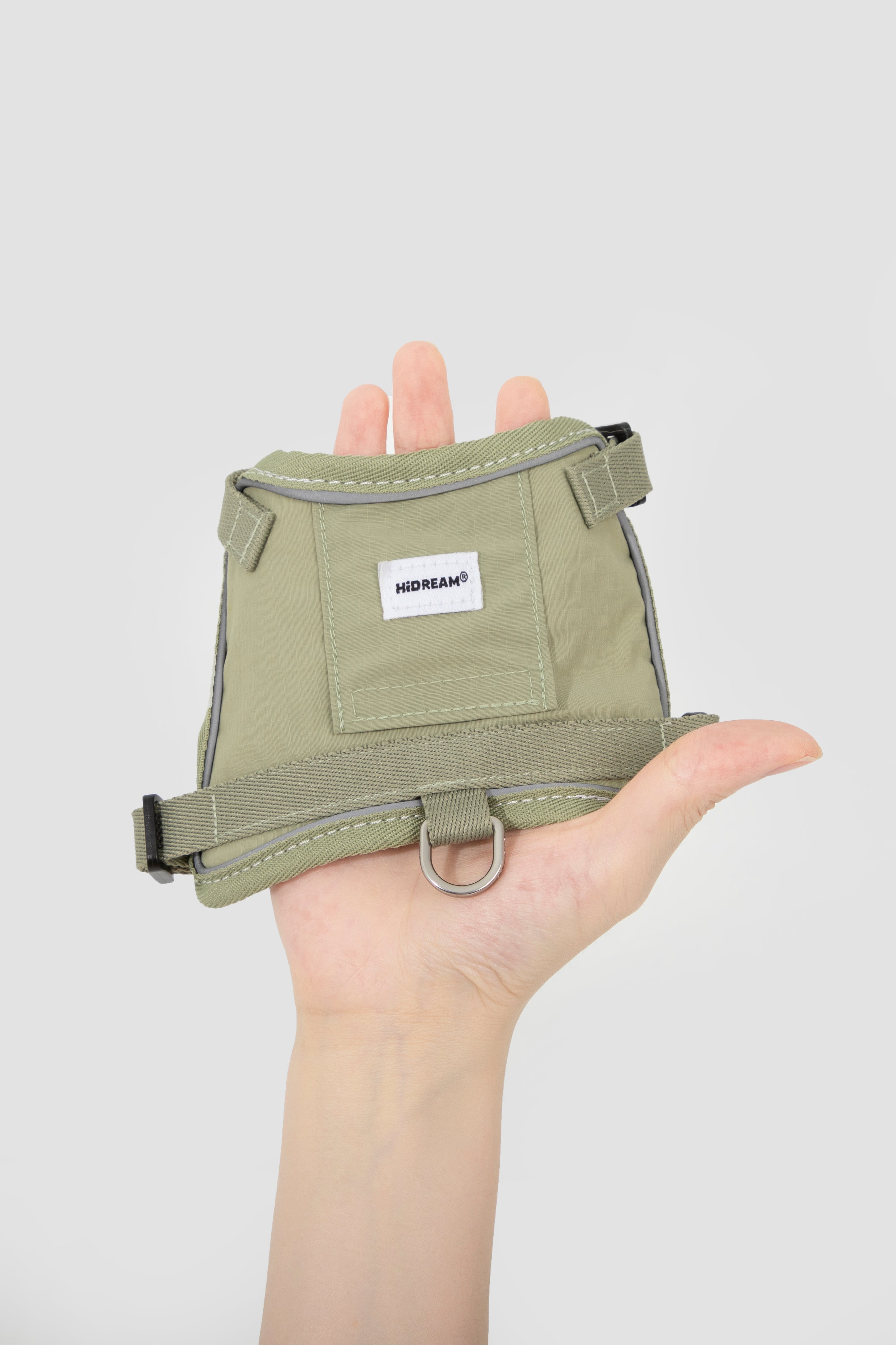 Green dog harness held in a hand against a white background