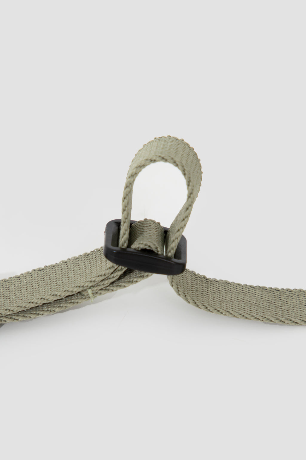 Close-up of a light olive green woven strap with a black plastic buckle, shown on a light gray background.