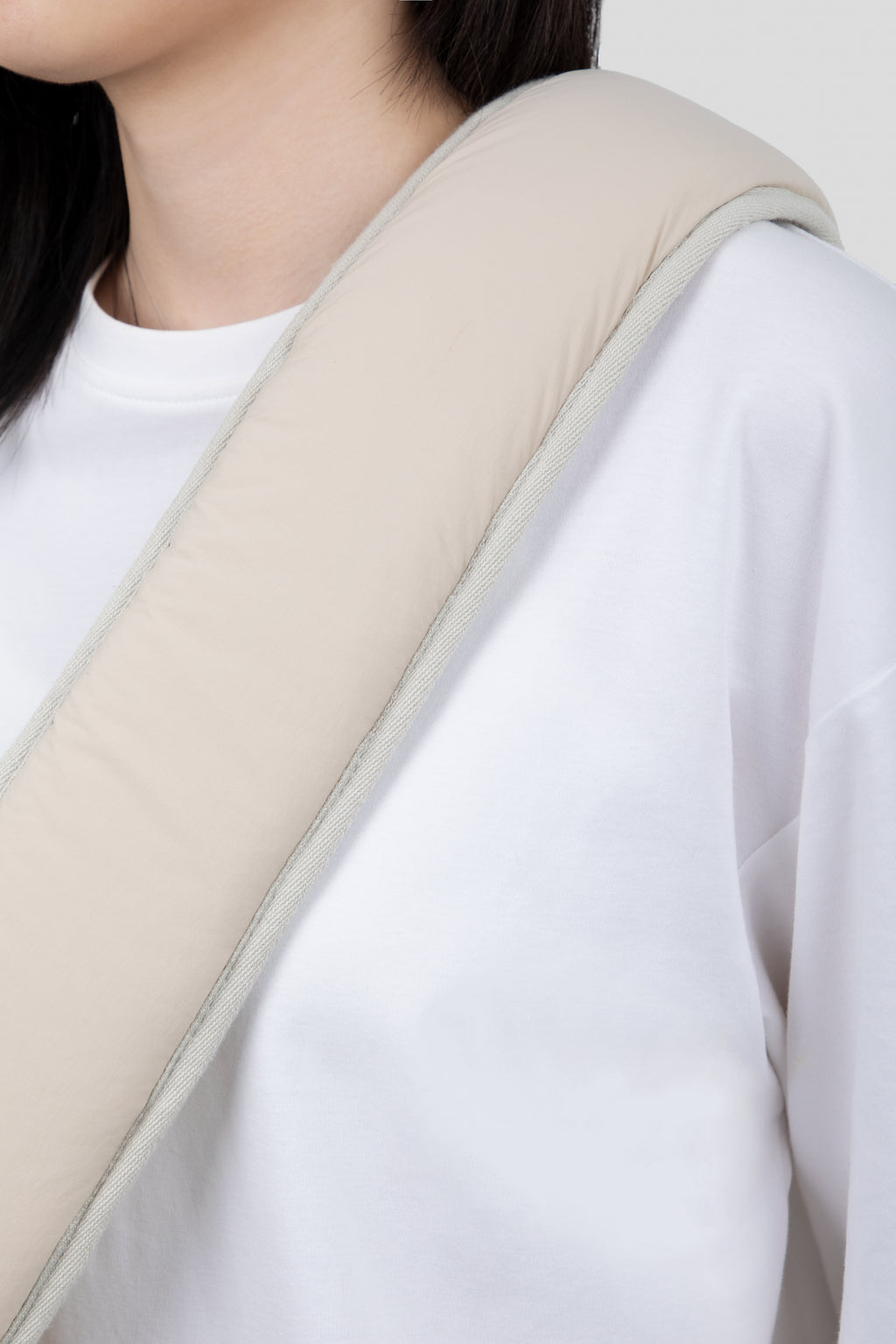 A close-up of a person wearing a white long-sleeve shirt with a beige padded shoulder support or neck pillow draped over the shoulder against a light gray background.