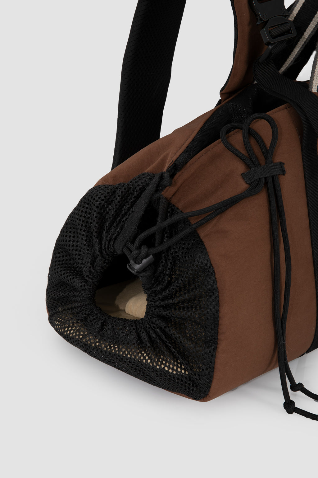 Close-up of a brown and black duffel bag showing a black mesh side pocket with drawstring closure, on a light gray background.