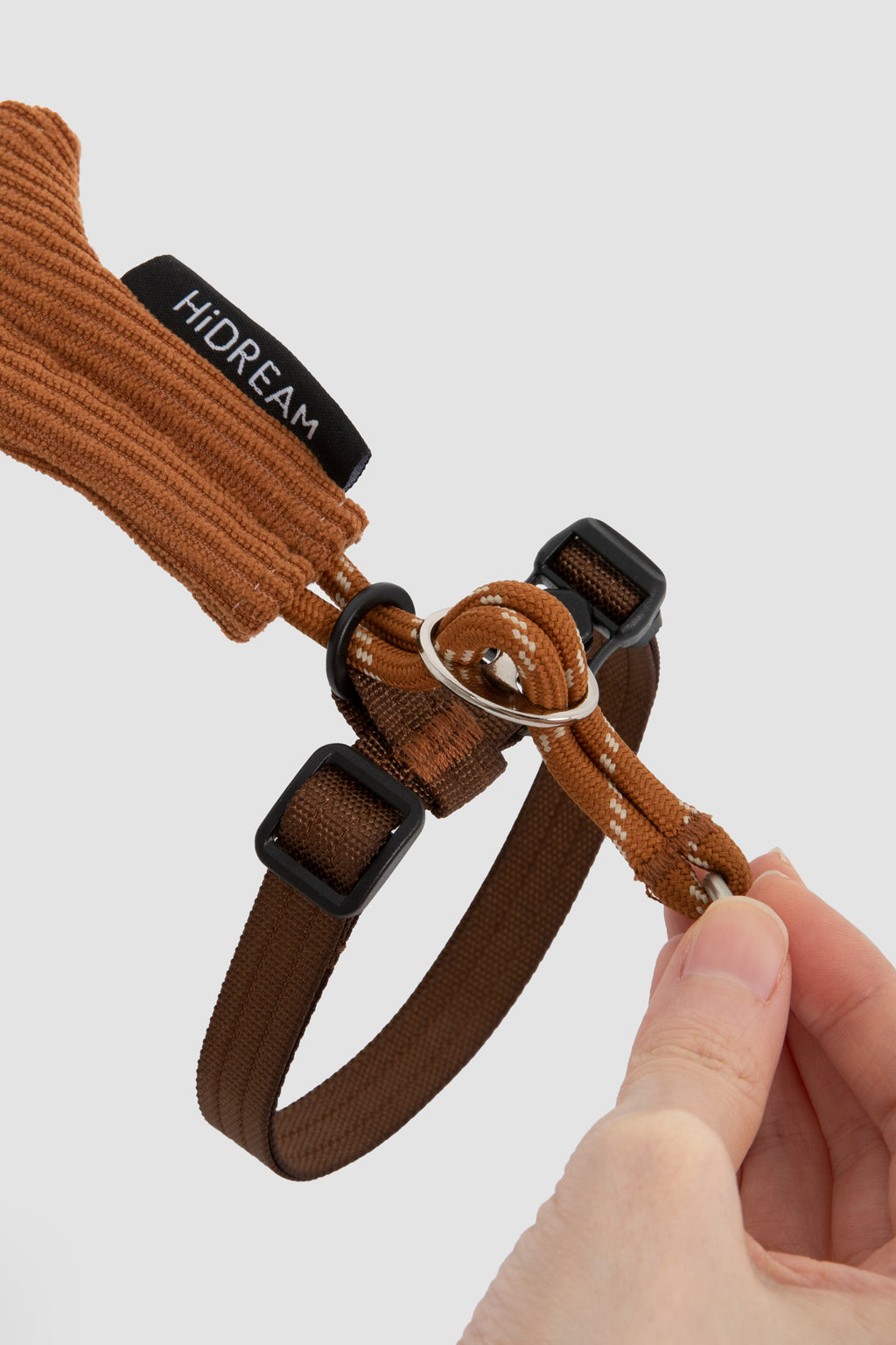 Brown cat harness with black hardware being adjusted on a light gray background