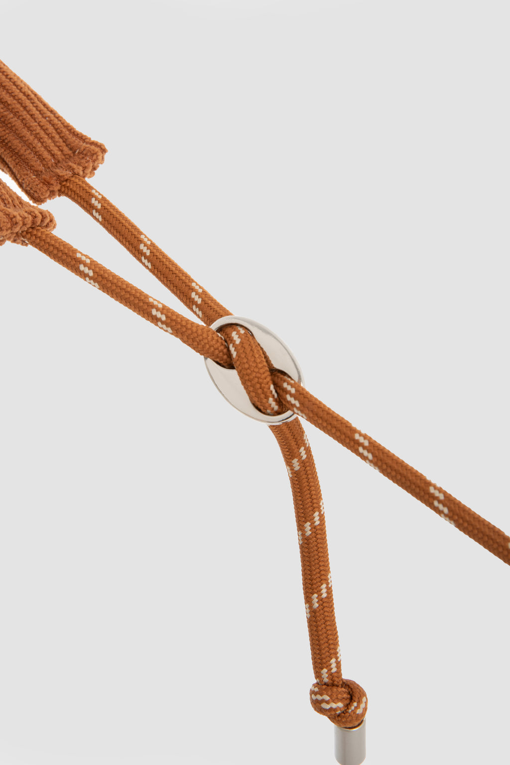 A close-up of a brown braided rope with white speckles and a silver metal ring, shown against a light gray background.