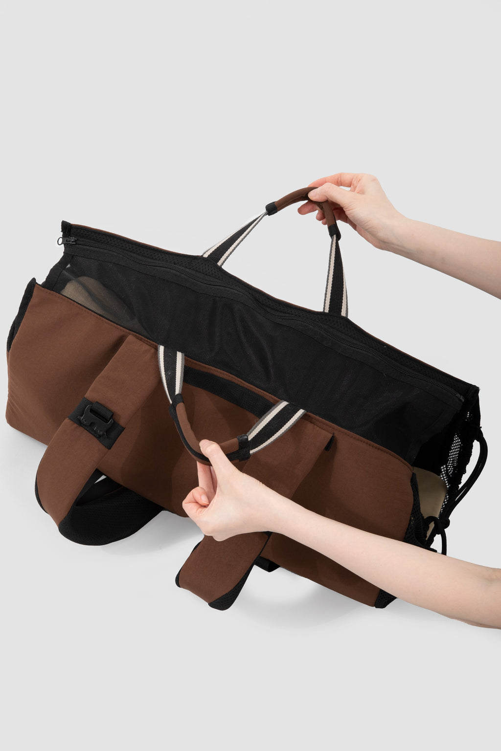 A brown and black duffel bag being held open by two hands against a light gray background.