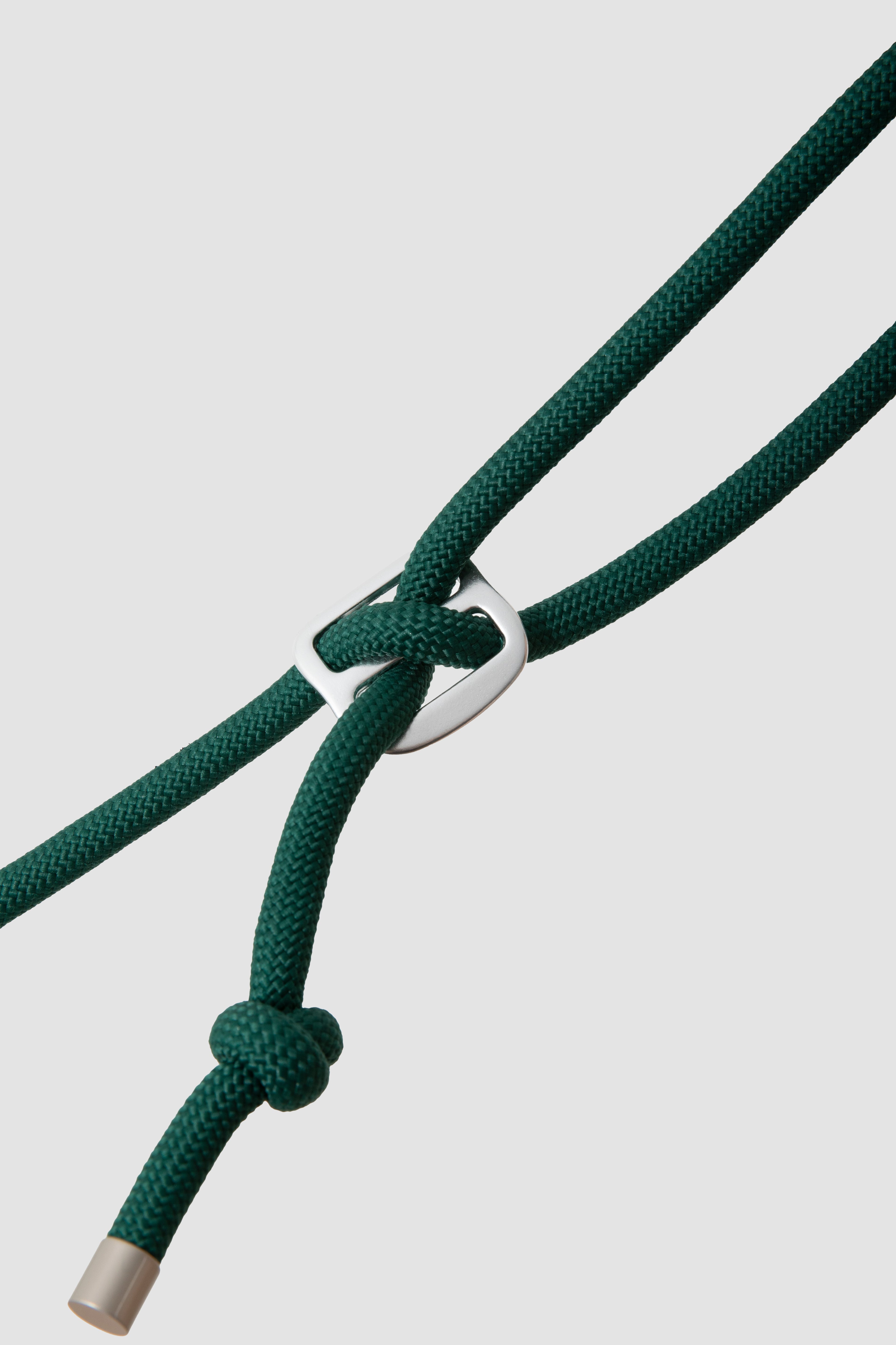 A close-up of a dark green braided cord necklace with a silver metal ring connector and a knotted end, shown against a light gray background.
