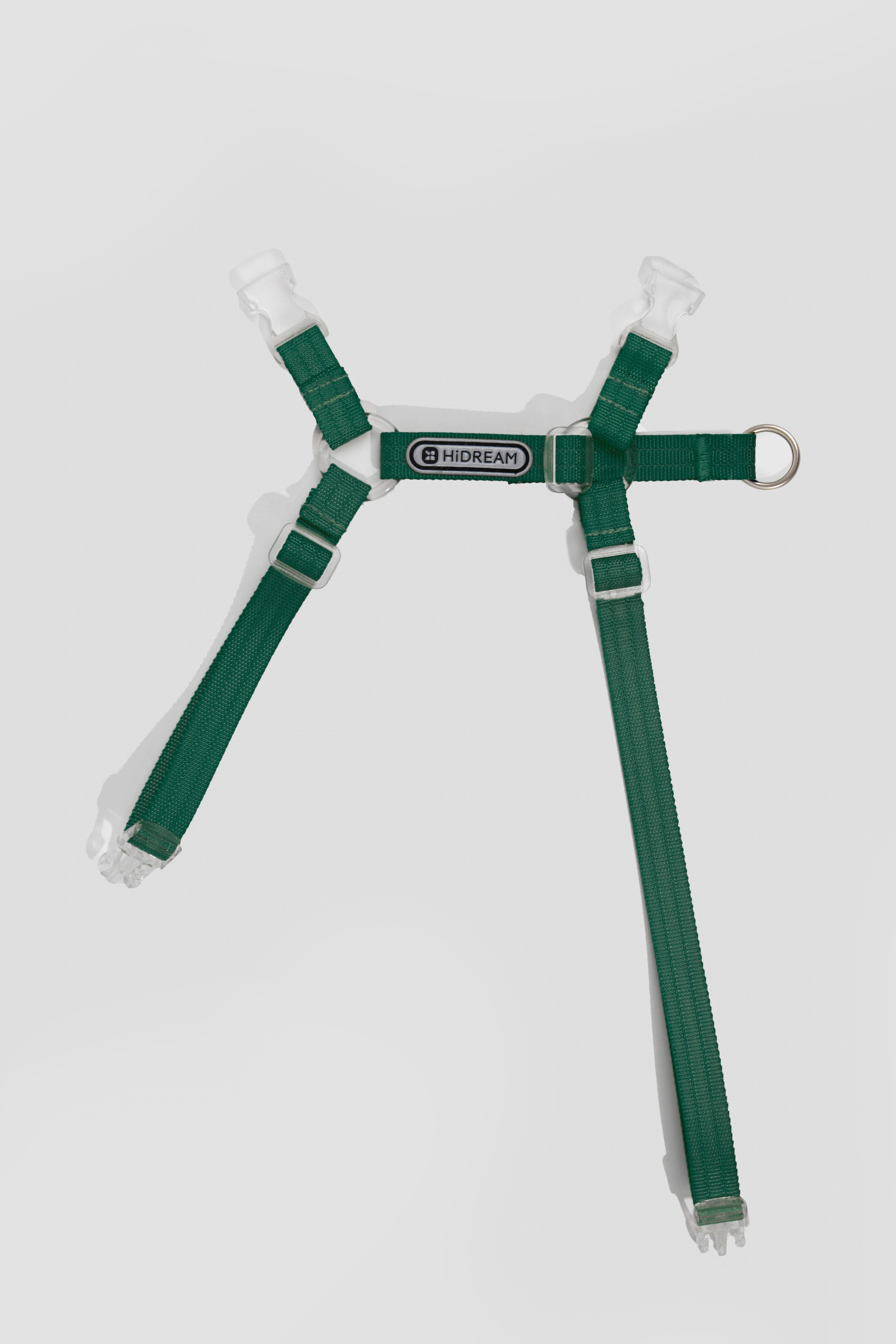 A green pet harness with white plastic buckles and a metal ring, shown against a light gray background.