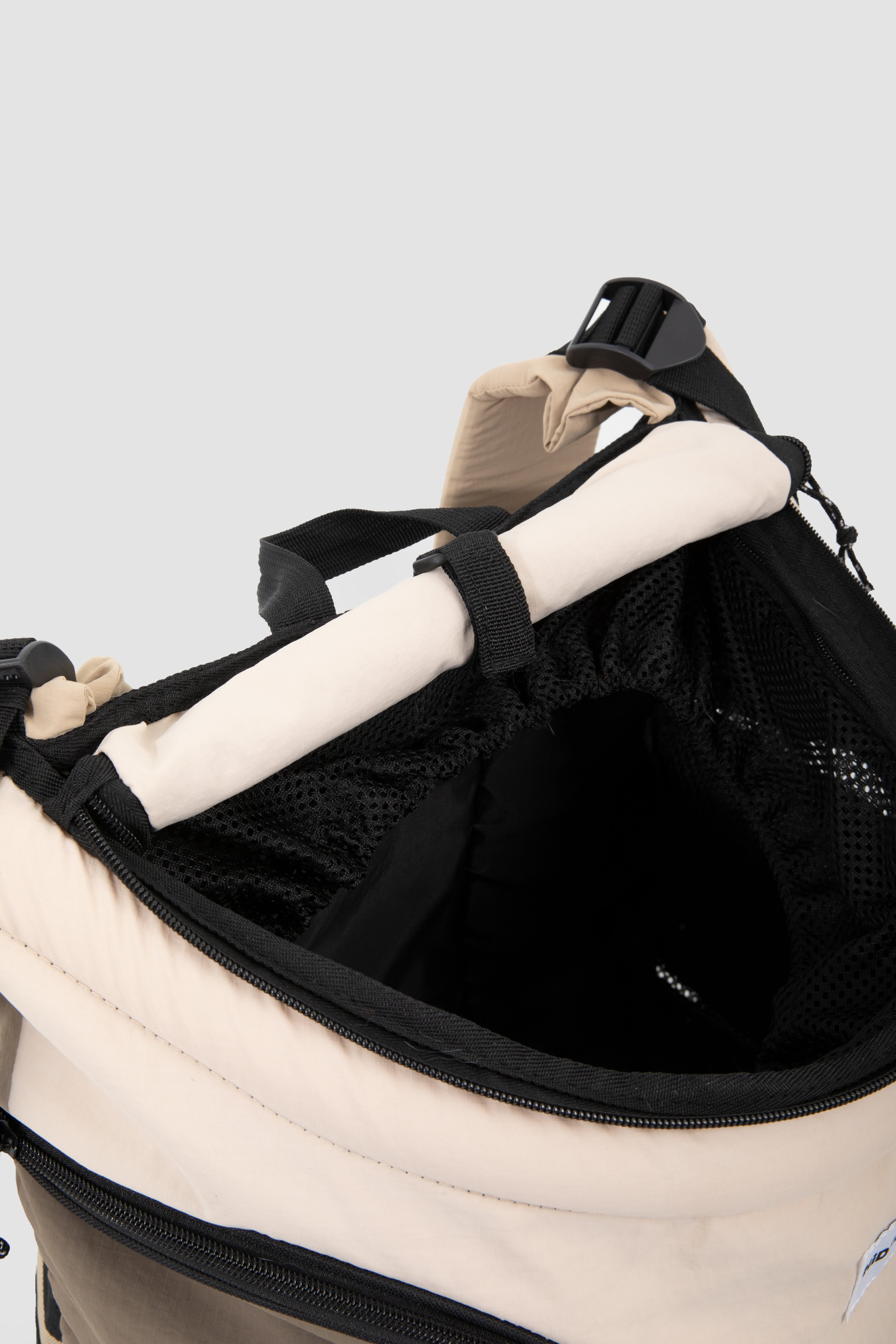 Close-up of a beige and black backpack opening, showing the interior mesh lining, black straps, and a rolled light-colored item secured inside.