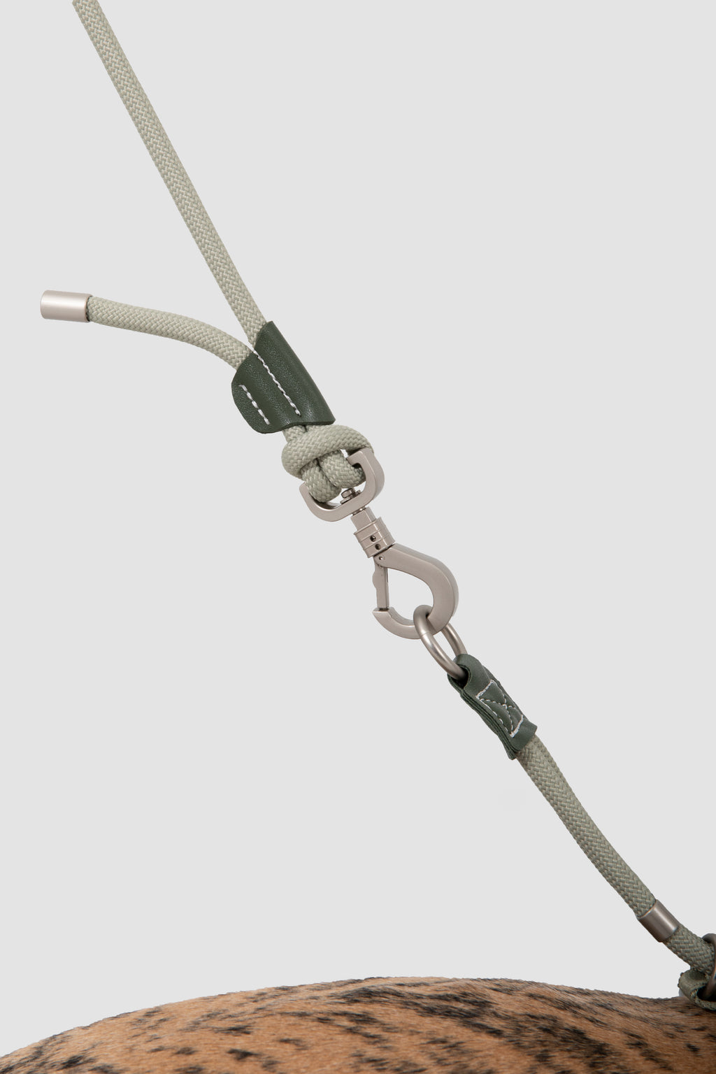 A close-up of a light gray rope lead with dark green leather wraps and silver metal hardware, shown attached to a dog's halter on a plain light gray background.