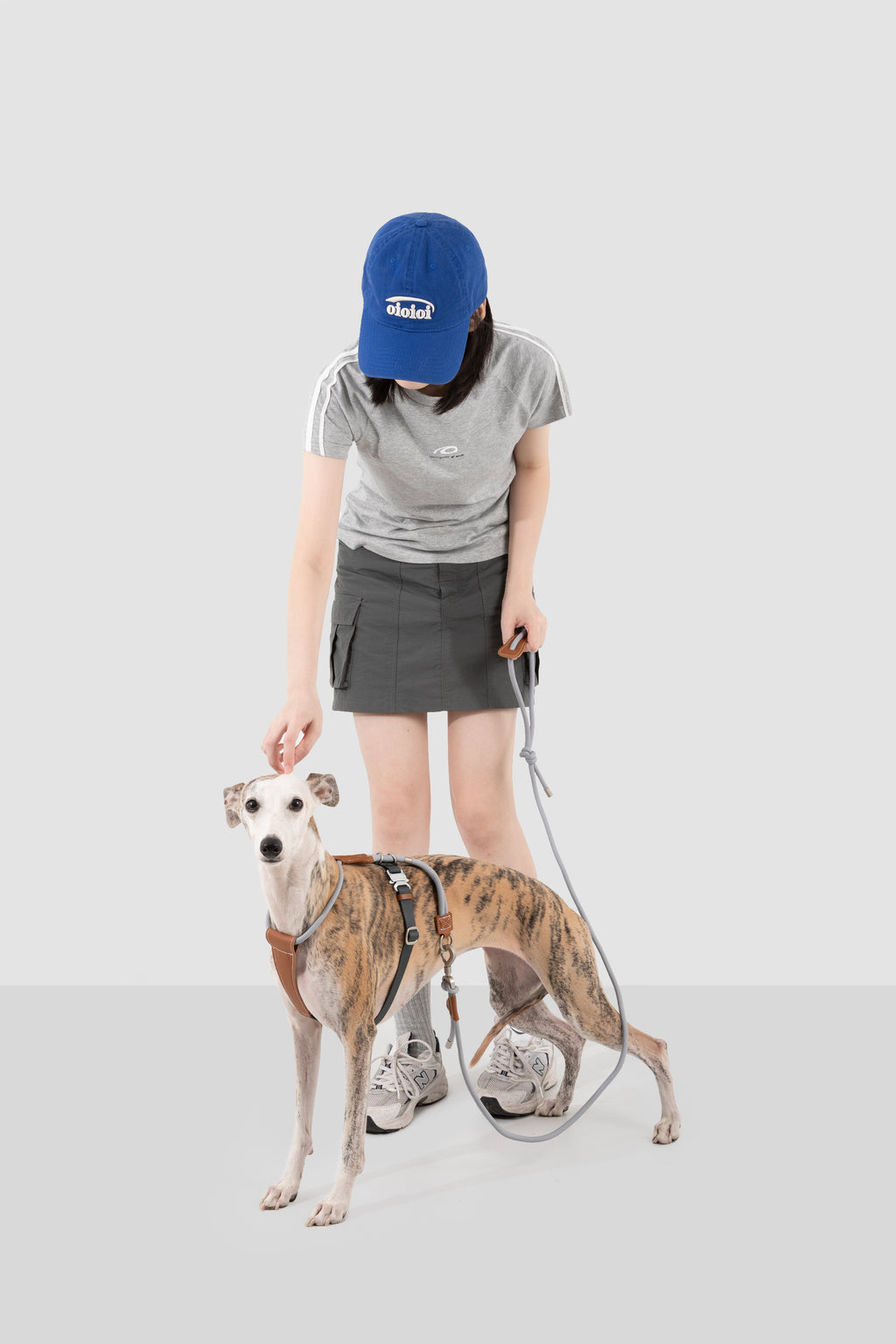 Person wearing a blue cap and gray shirt with a dog on a white background