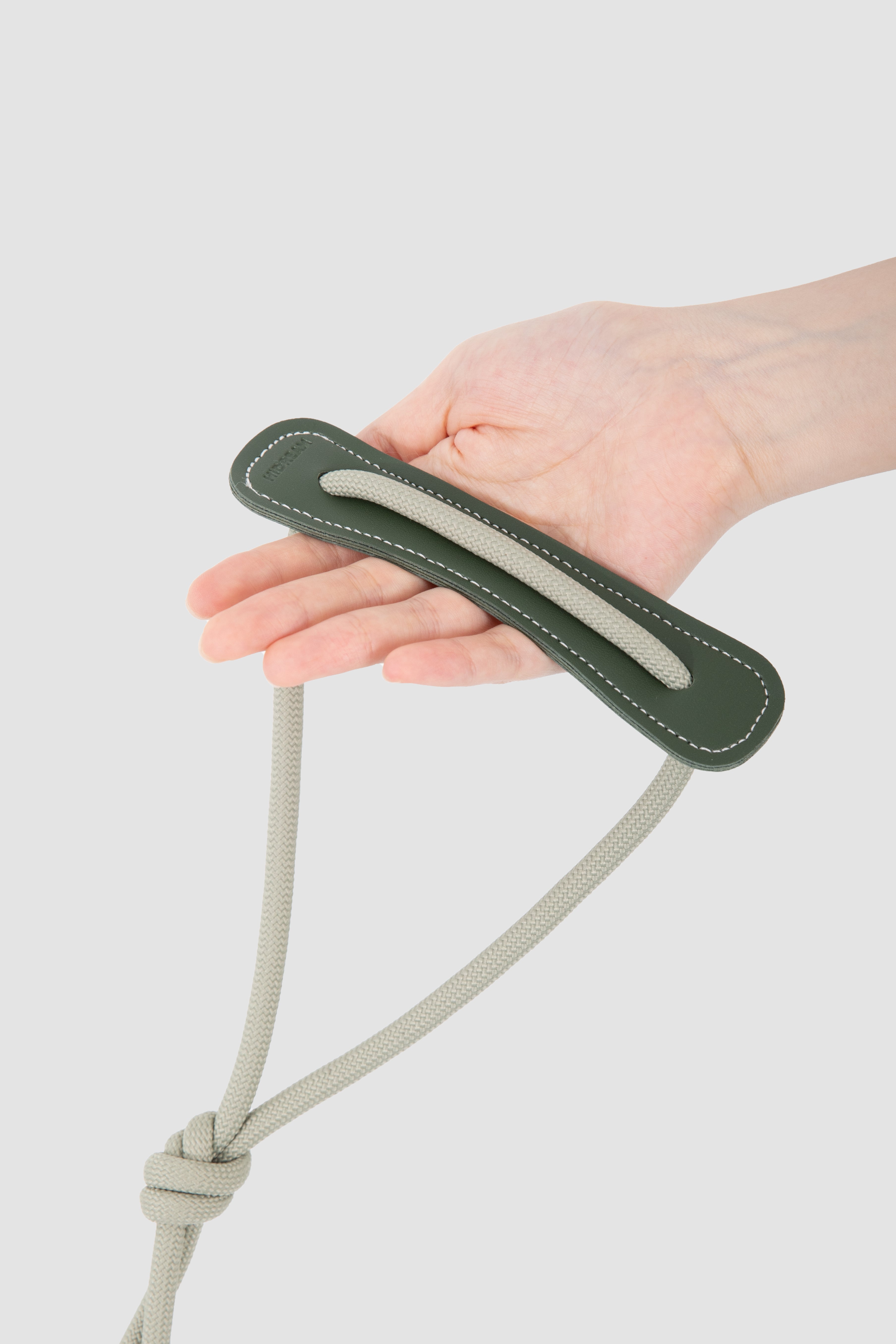 Hand holding a green leather strap with a white background
