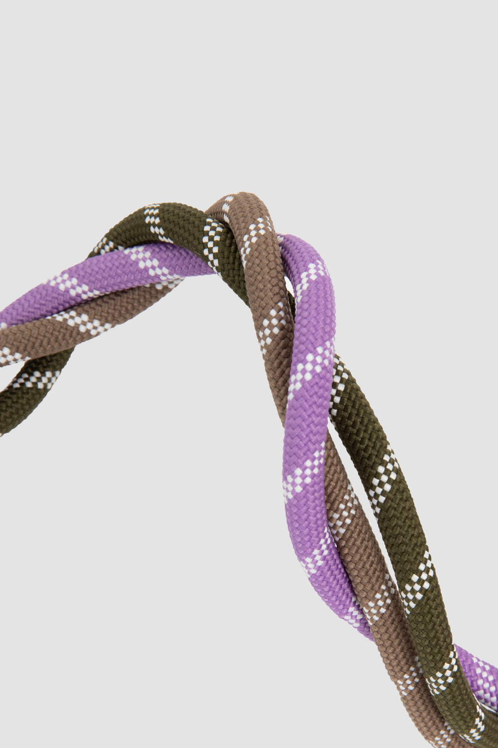 A close-up of a braided rope or cord with three twisted strands in olive green, brown, and purple, each with small white dotted accents, set against a light gray background.