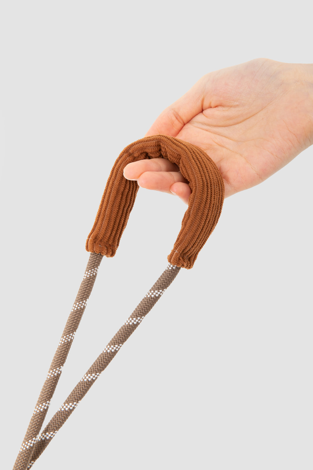 A close-up of a hand holding a brown ribbed rope handle with two braided brown-and-white rope leads against a light gray background.