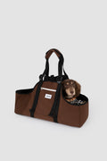 A brown and black pet carrier duffel bag with a small dachshund peeking out of the top compartment, set against a solid light gray background.