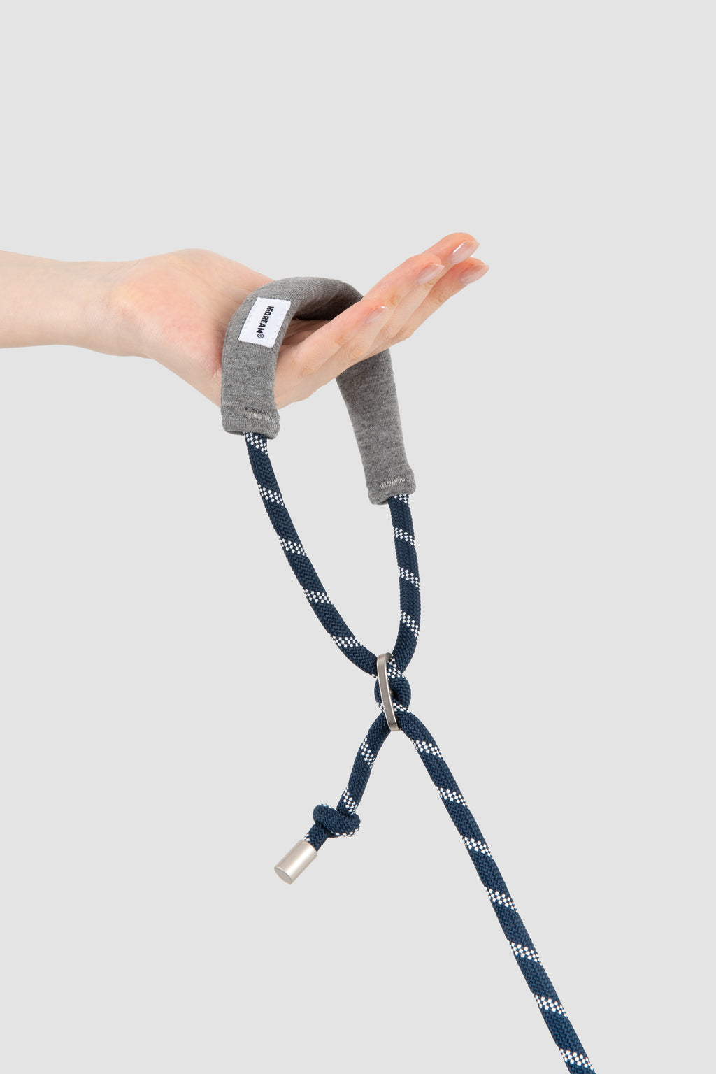 A hand holding a gray fabric wrist strap attached to a navy blue rope with white zigzag pattern and a silver metal tip, shown against a light gray background.