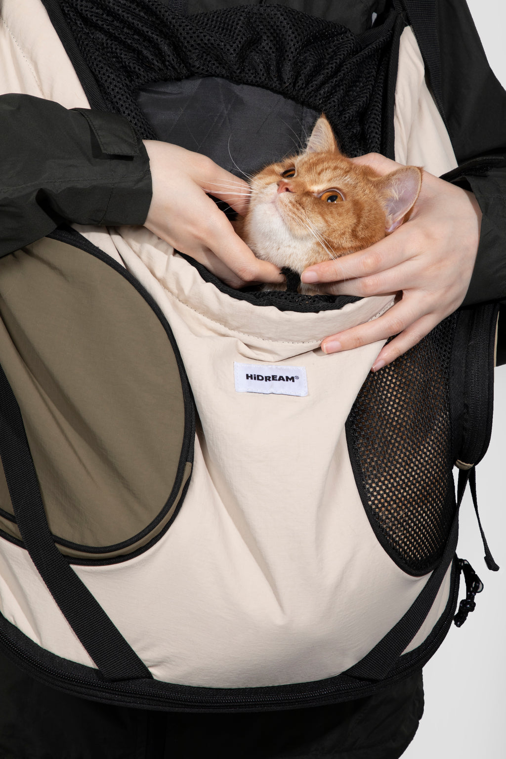 Person holding a cat in a beige pet carrier with a visible brand label.