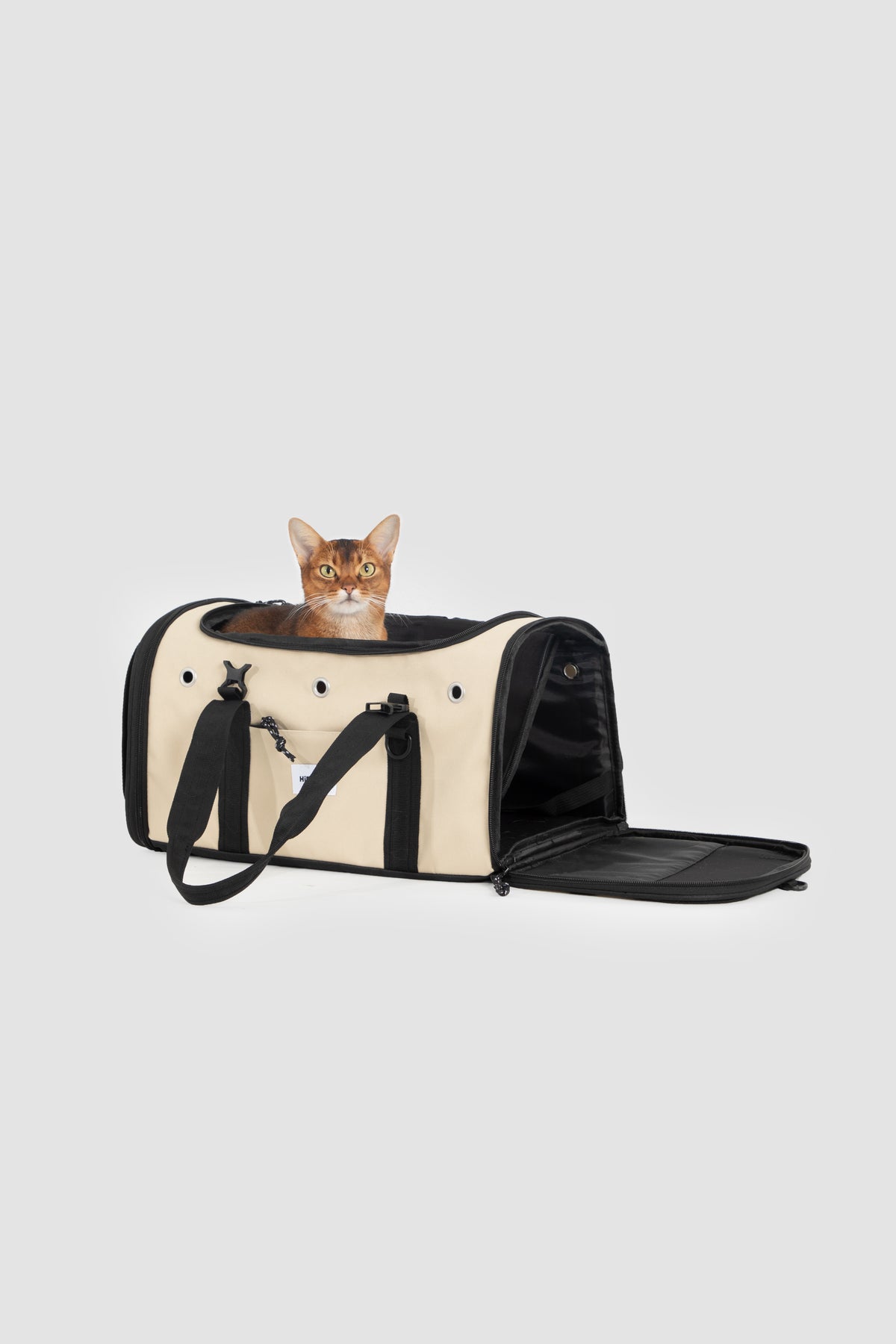 A cream and black pet carrier bag with an open front panel, shown on a light gray background with a small cat peeking out from the top.