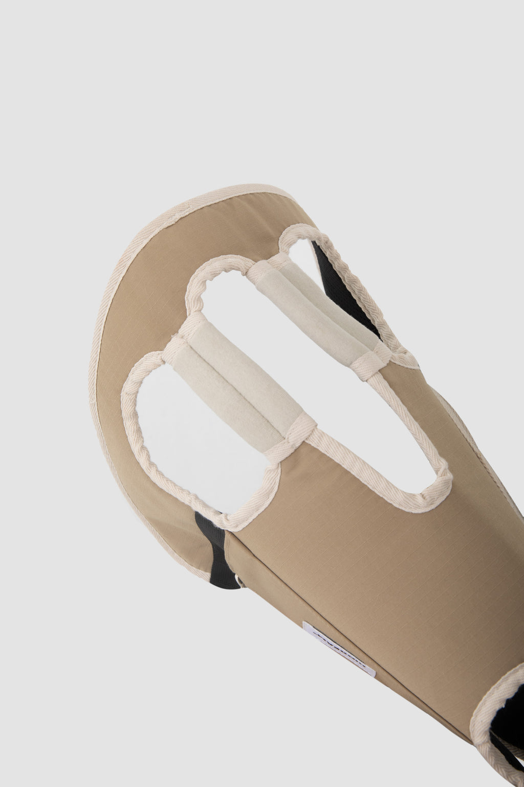 Close-up of a beige padded support or brace with white trim and black inner lining, shown against a light gray background.