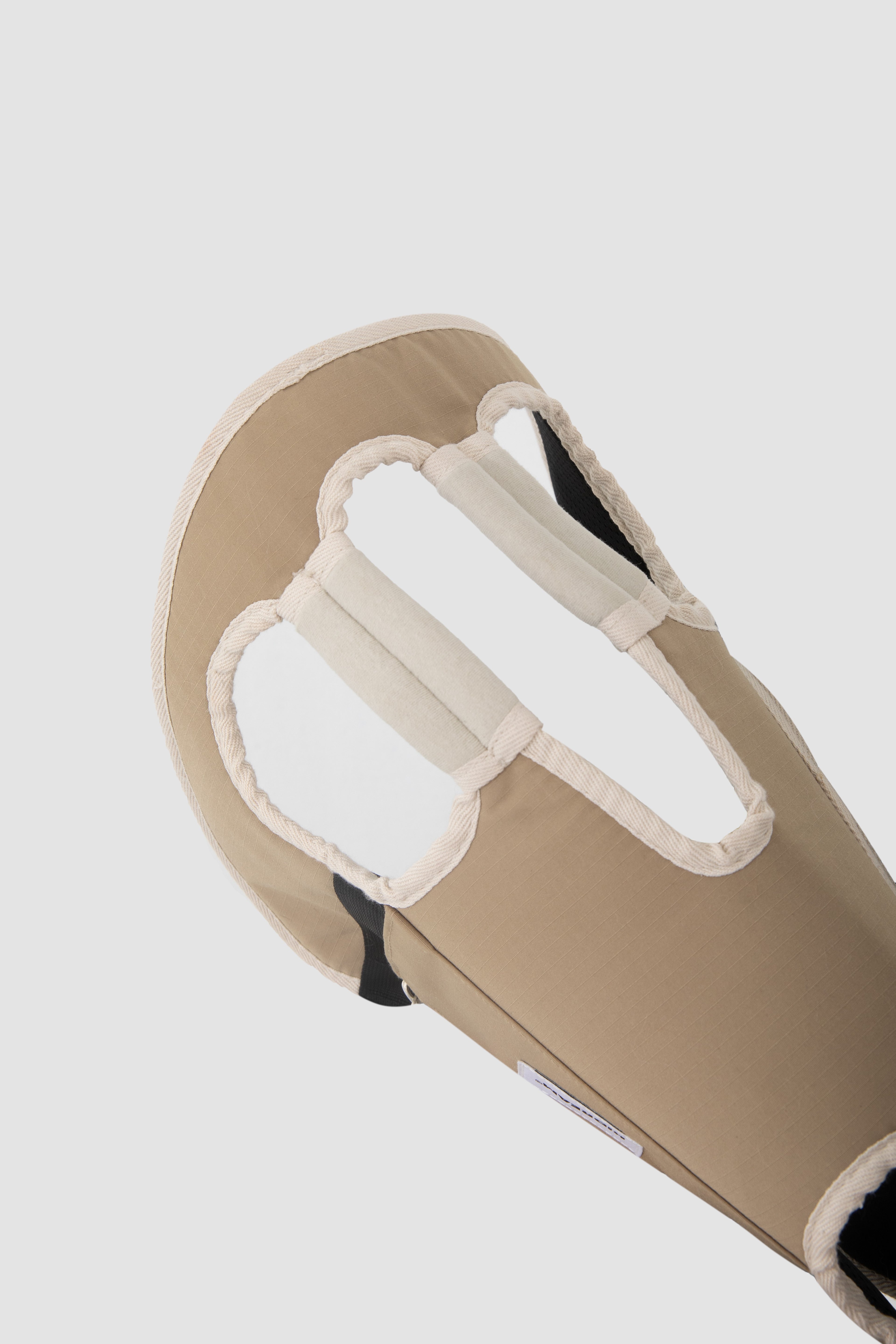 Close-up of a beige padded support or brace with white trim and black inner lining, shown against a light gray background.