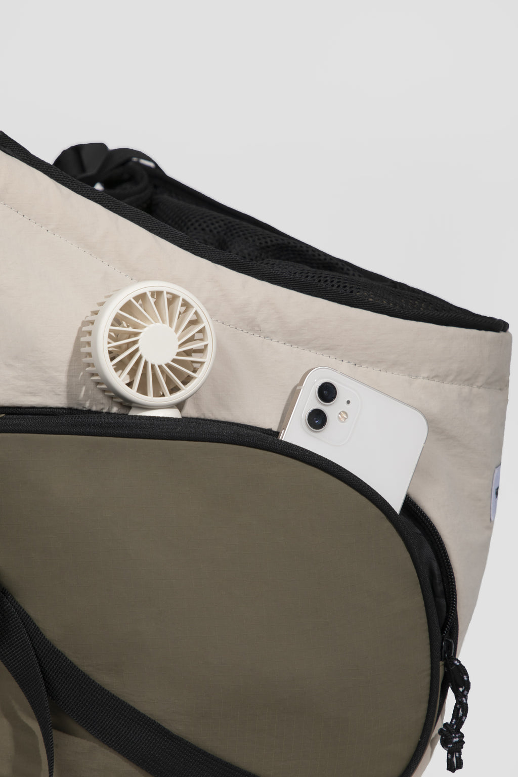 Close-up of a beige and olive green utility bag with black trim, showing a white mini fan and a white smartphone tucked into the side pocket.