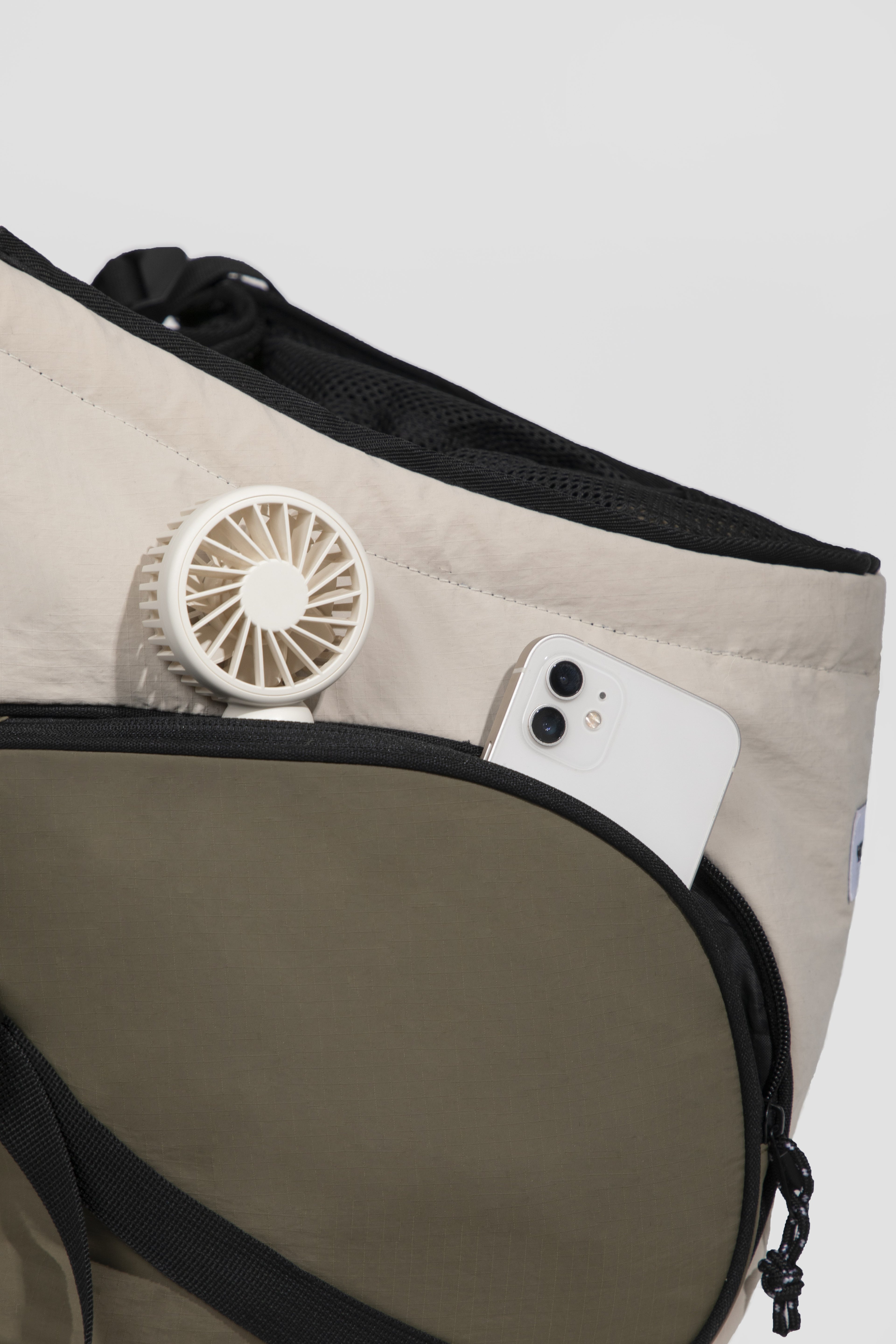 Close-up of a beige and olive green utility bag with black trim, showing a white mini fan and a white smartphone tucked into the side pocket.