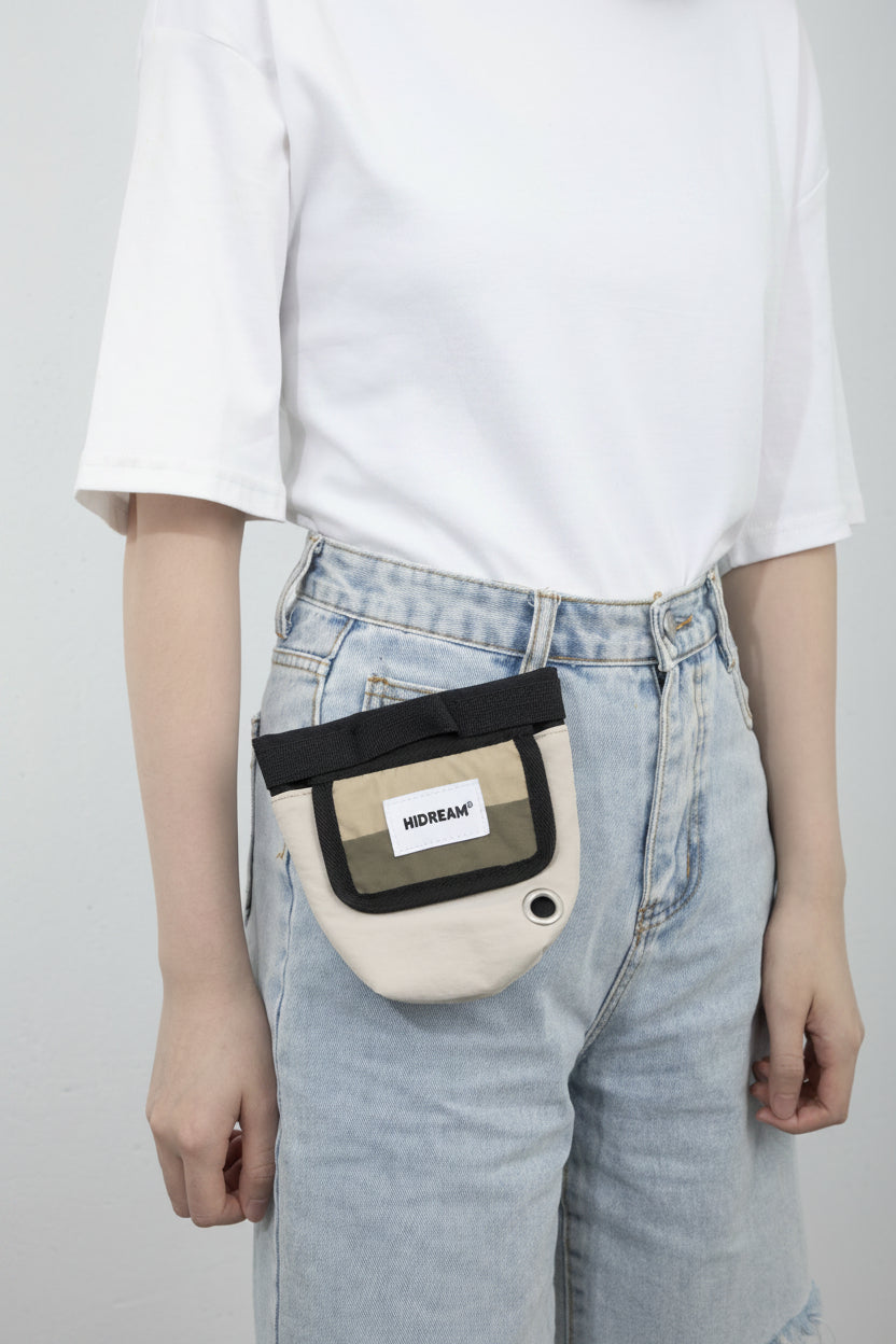 A person wearing a white T-shirt with black Chinese text and light-wash denim shorts, carrying a beige and black utility pouch at the front of the waist. The pouch has a white label reading 'HiDREAM'.