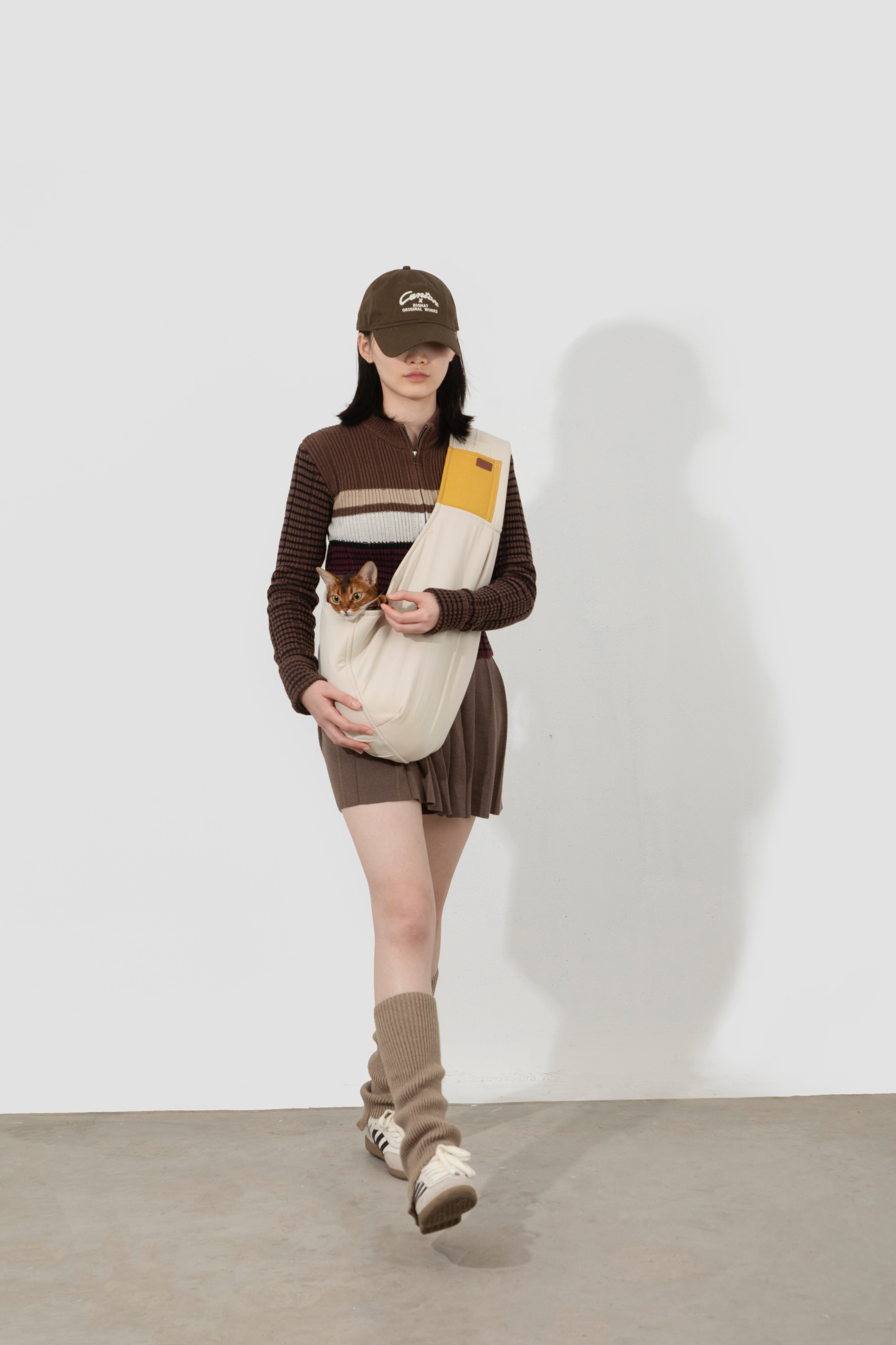 Person wearing a brown outfit with a beige bag and cap, standing against a white background