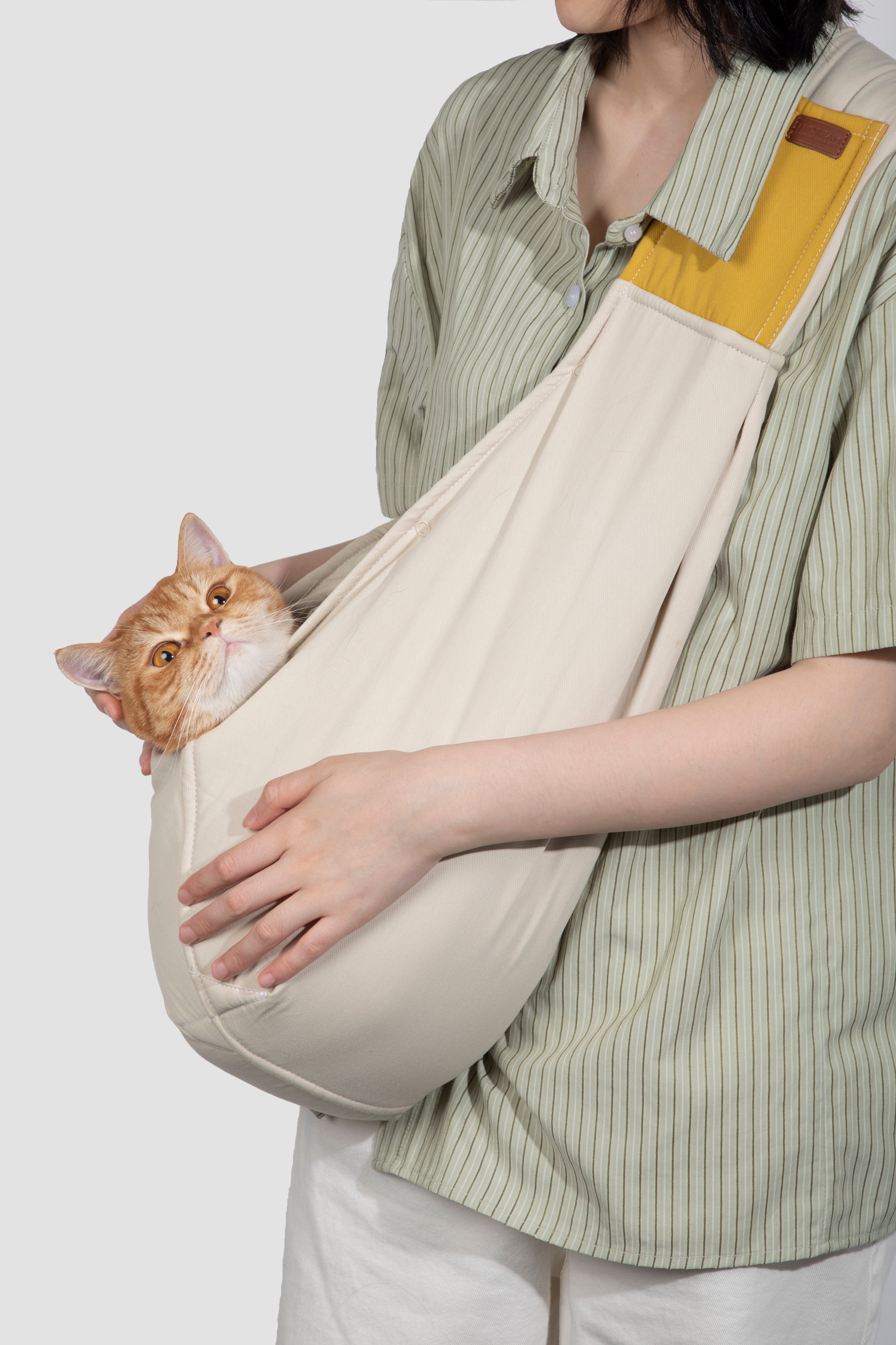 Person holding a cat in a beige sling against a plain background