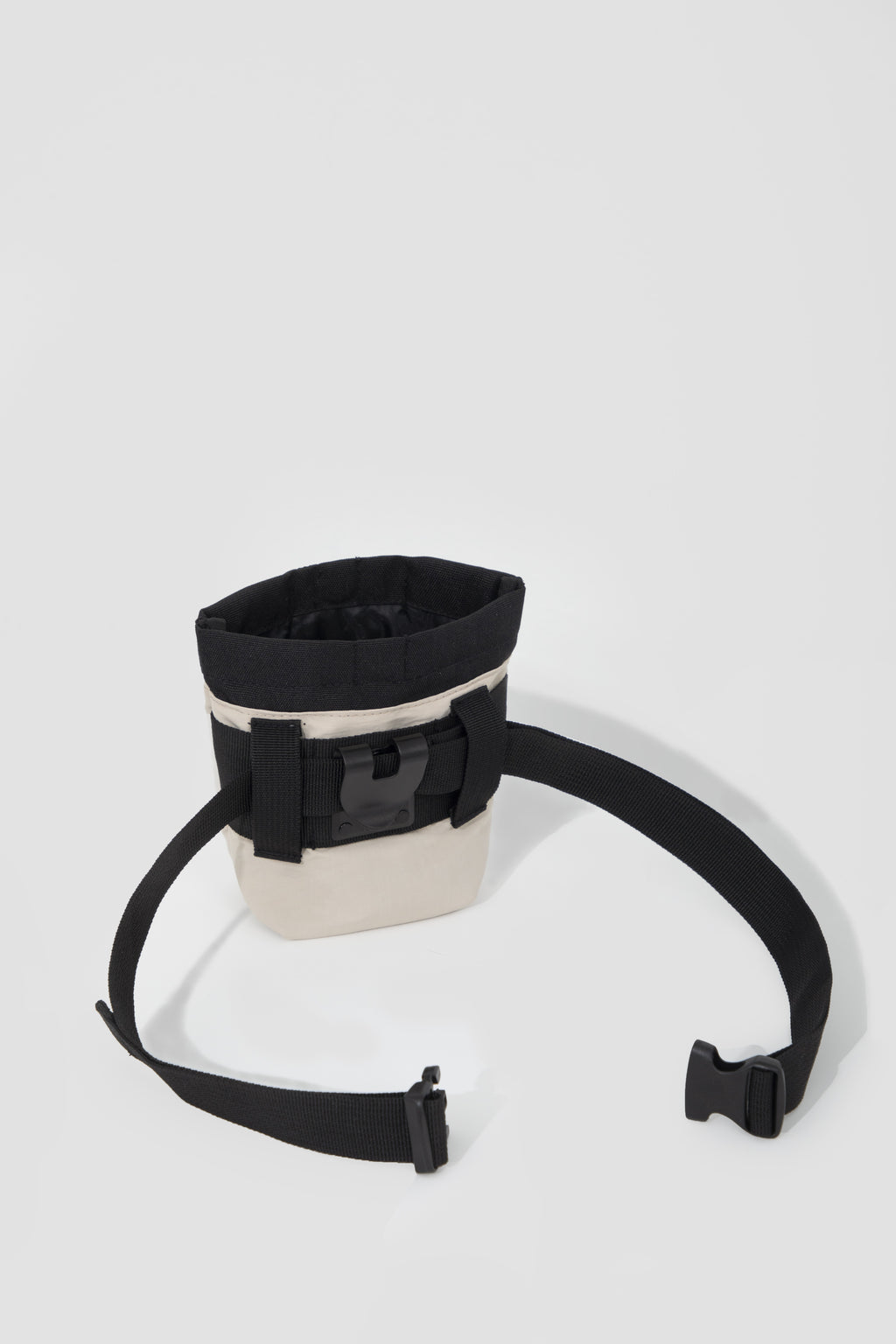 A black and off-white fabric pouch with an adjustable black strap and plastic buckle, photographed on a light gray studio background.