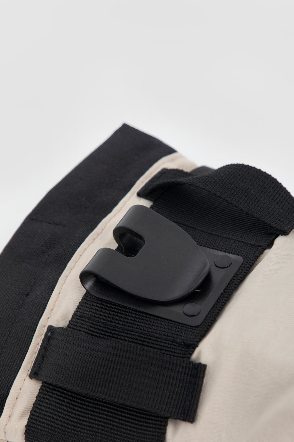 Close-up of a black plastic quick-release buckle attached to a black webbing strap on a light beige fabric surface, photographed against a plain light background.