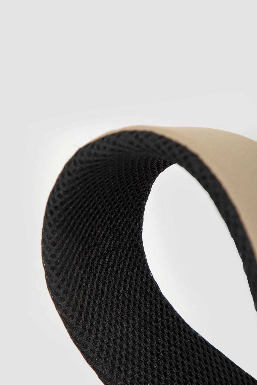 Close-up of a curved black mesh band with a beige outer edge on a light gray background.