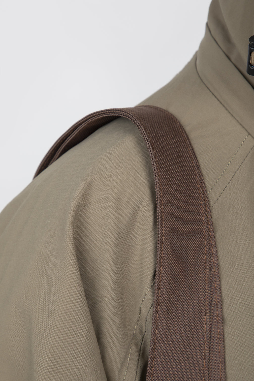 Close-up of a khaki jacket with a brown shoulder strap, likely from a bag or accessory, draped over the shoulder.