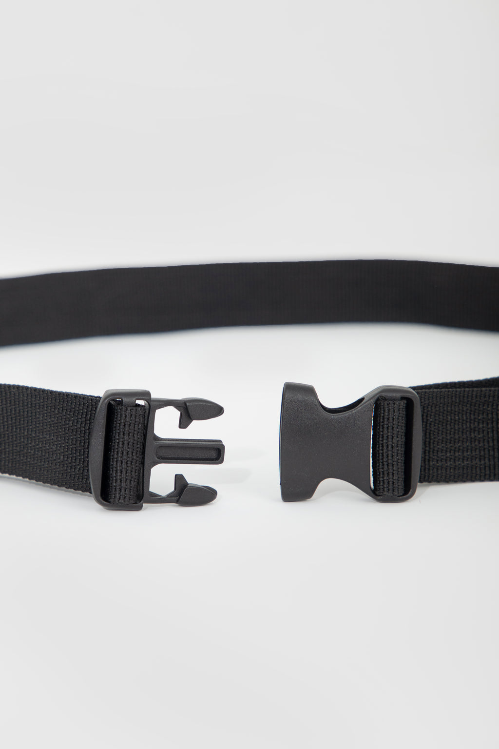 A close-up of a black web belt showing both sides of the buckle mechanism against a light gray background.