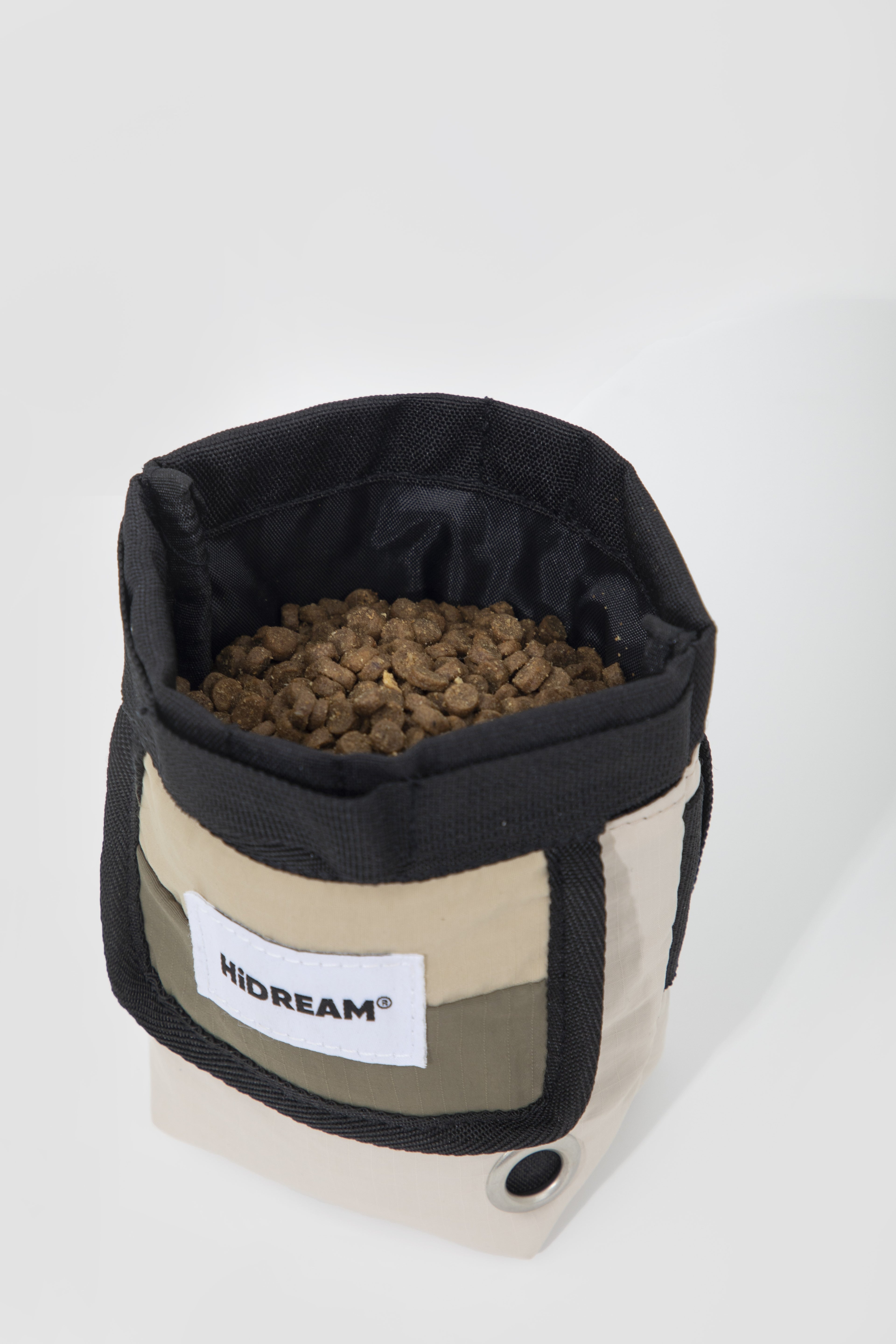 A fabric pet bowl by HiDREAM, filled with brown kibble, set against a plain light gray background.