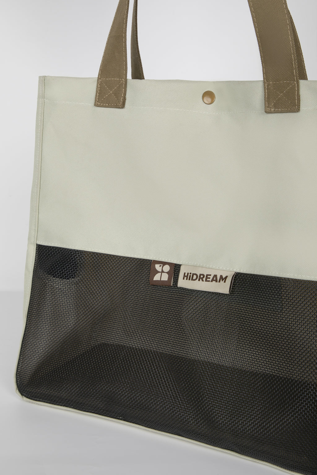 A large tote bag with a light beige upper section, brown shoulder straps, and a black mesh lower pocket. A small brand label reading HIDREAM is visible on the front.