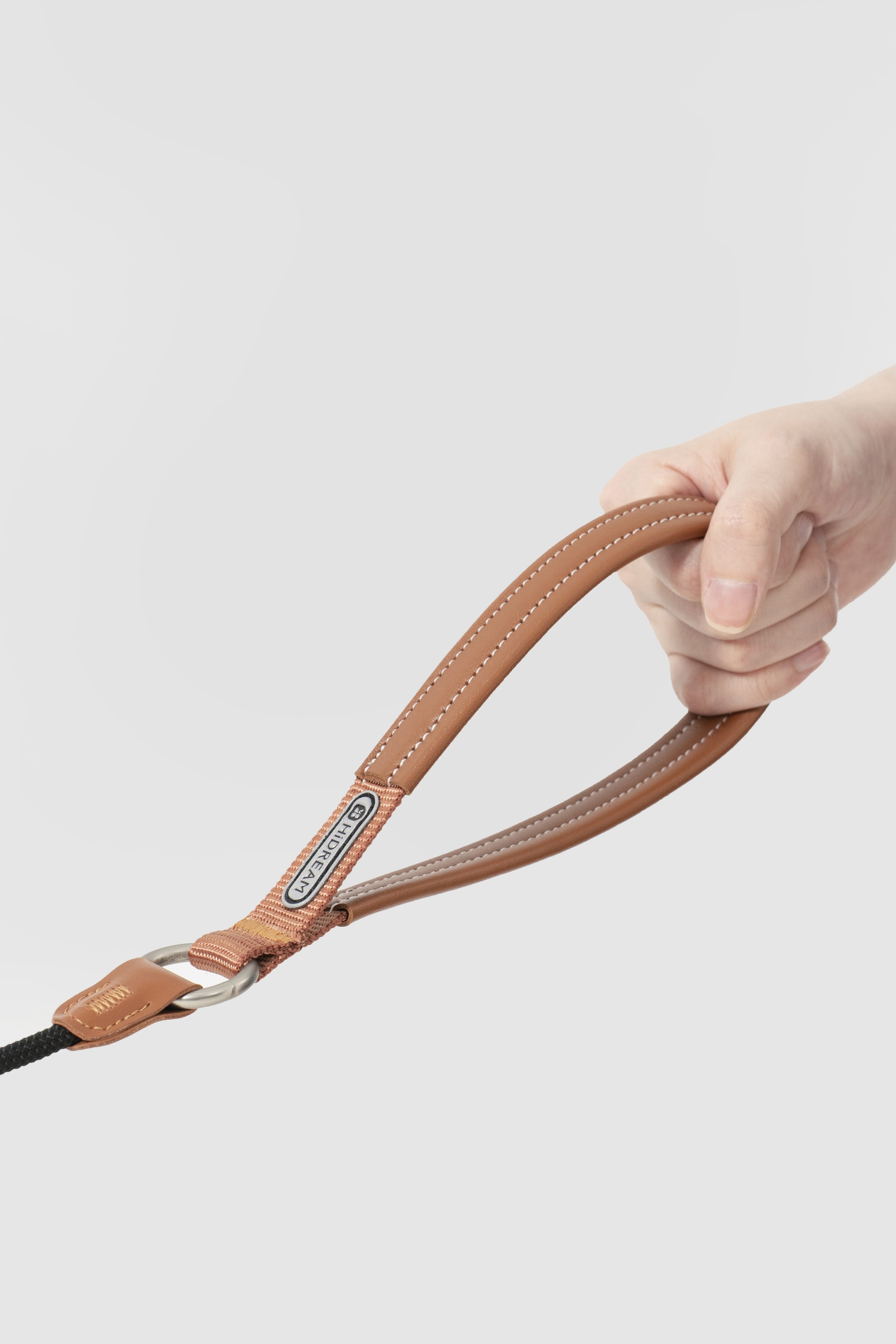 Hand holding a brown leather camera strap against a light gray background