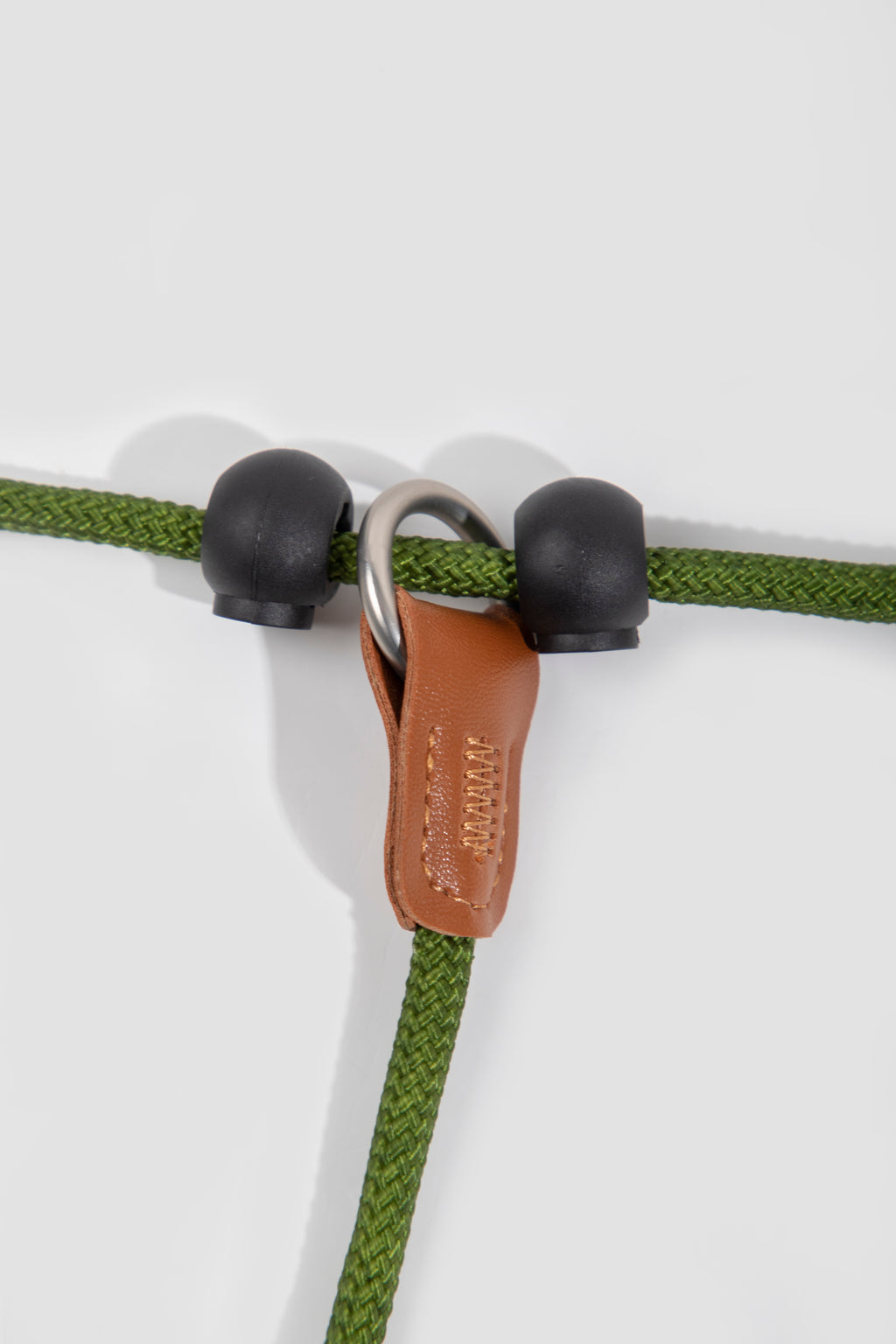 Close-up of green rope with black eyelets and a brown leather clip on a white background