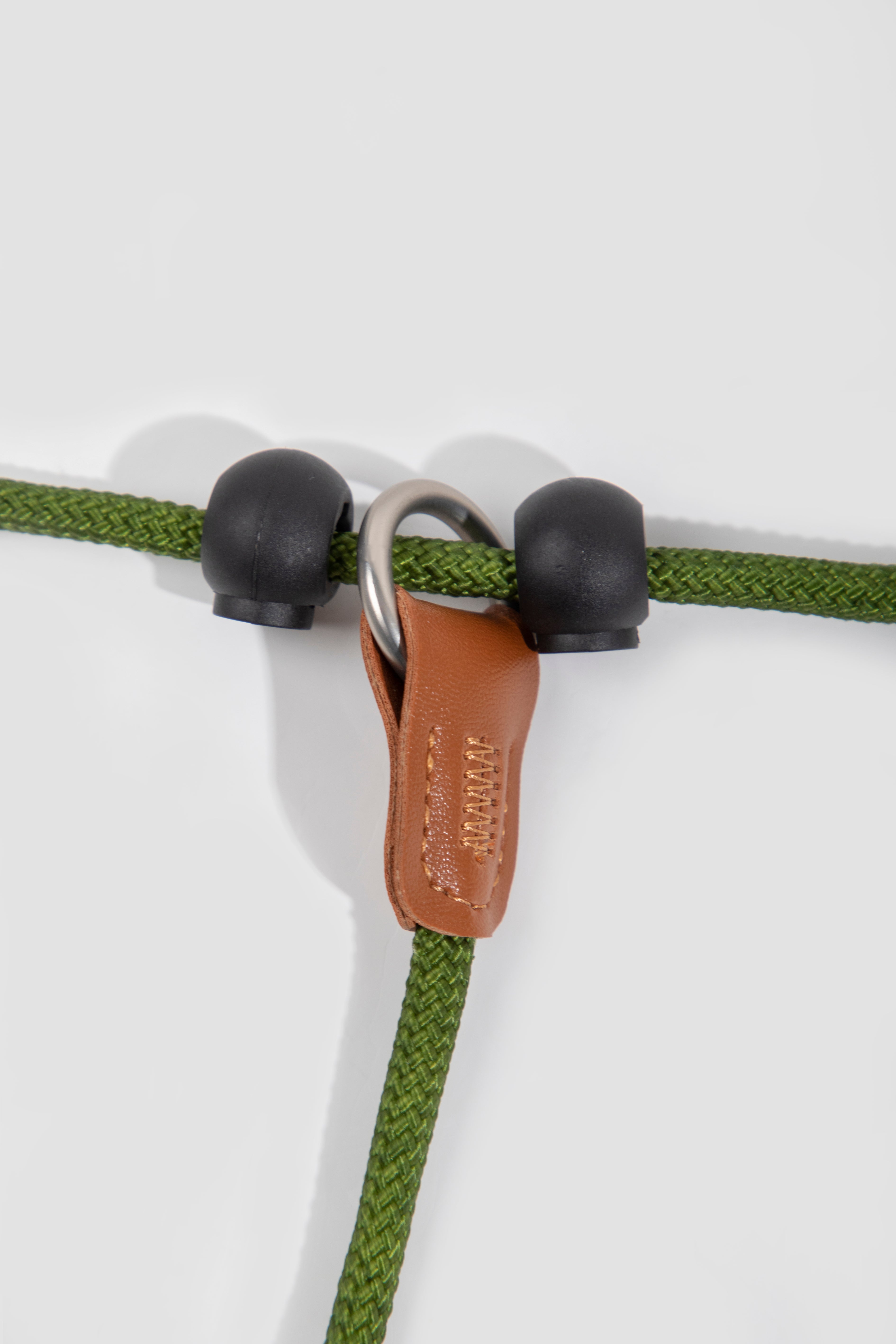 Close-up of green rope with black eyelets and a brown leather clip on a white background
